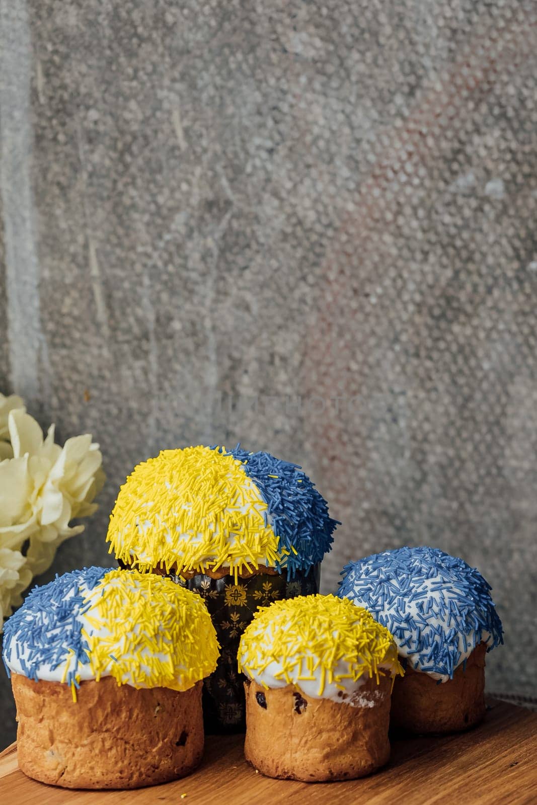 Delicious Easter cakes in the colors of the flag of Ukraine, yellow and blue on a wooden table with flowers in the background. place for text. selective focus by Anyatachka