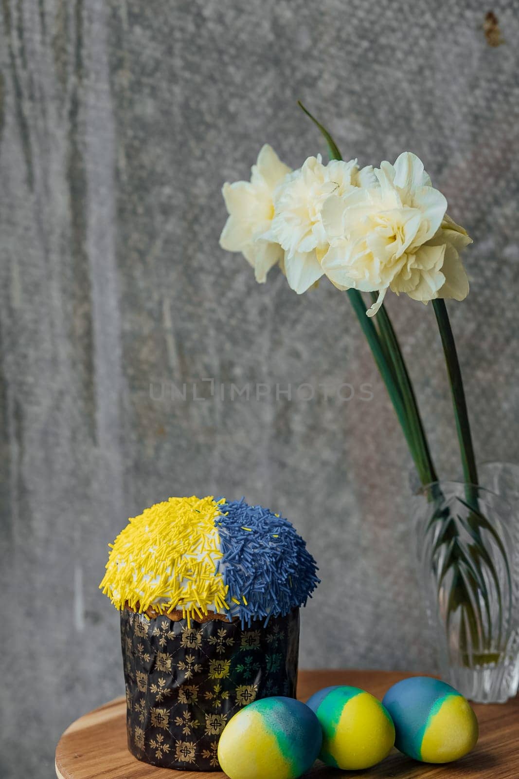 Delicious Easter cake in the colors of the flag of Ukraine, yellow-blue colored Easter eggs on a wooden table with flowers in the background. place for text. selective focus.