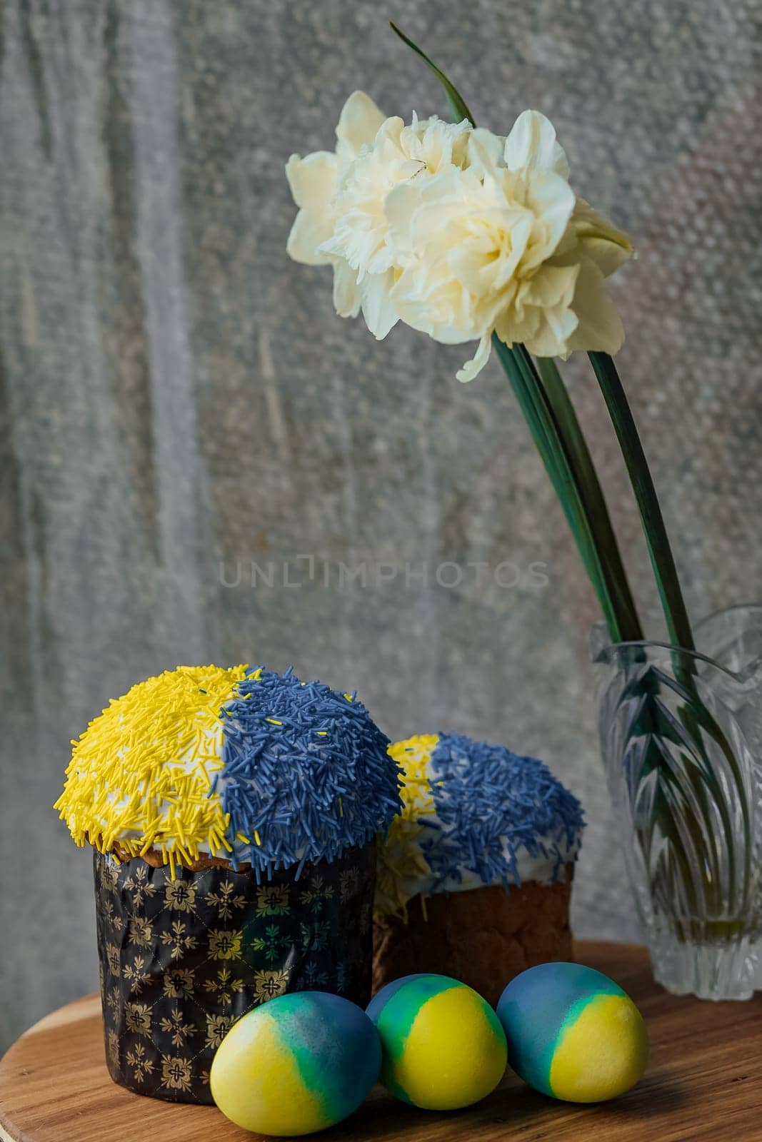Delicious Easter cake in the colors of the flag of Ukraine, yellow-blue colored Easter eggs on a wooden table with flowers in the background. place for text. selective focus.