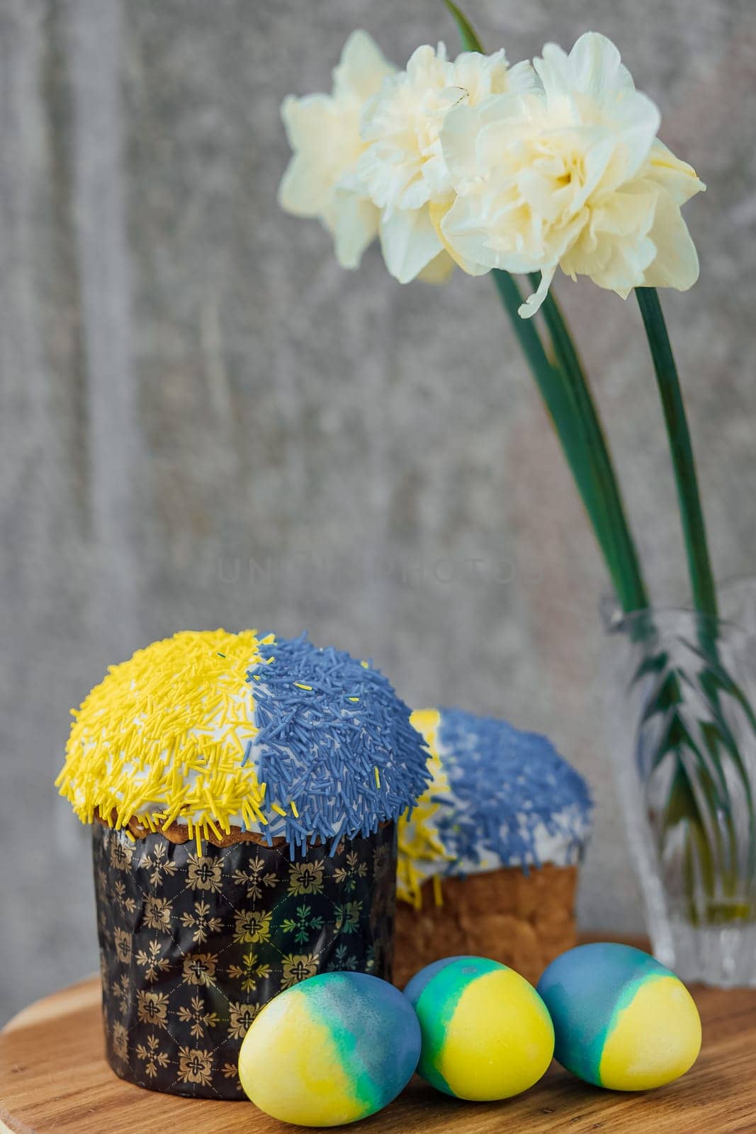 Delicious Easter cakes in the colors of the flag of Ukraine, yellow-blue colored Easter eggs on a wooden table with flowers in the background. place for text. selective focus.