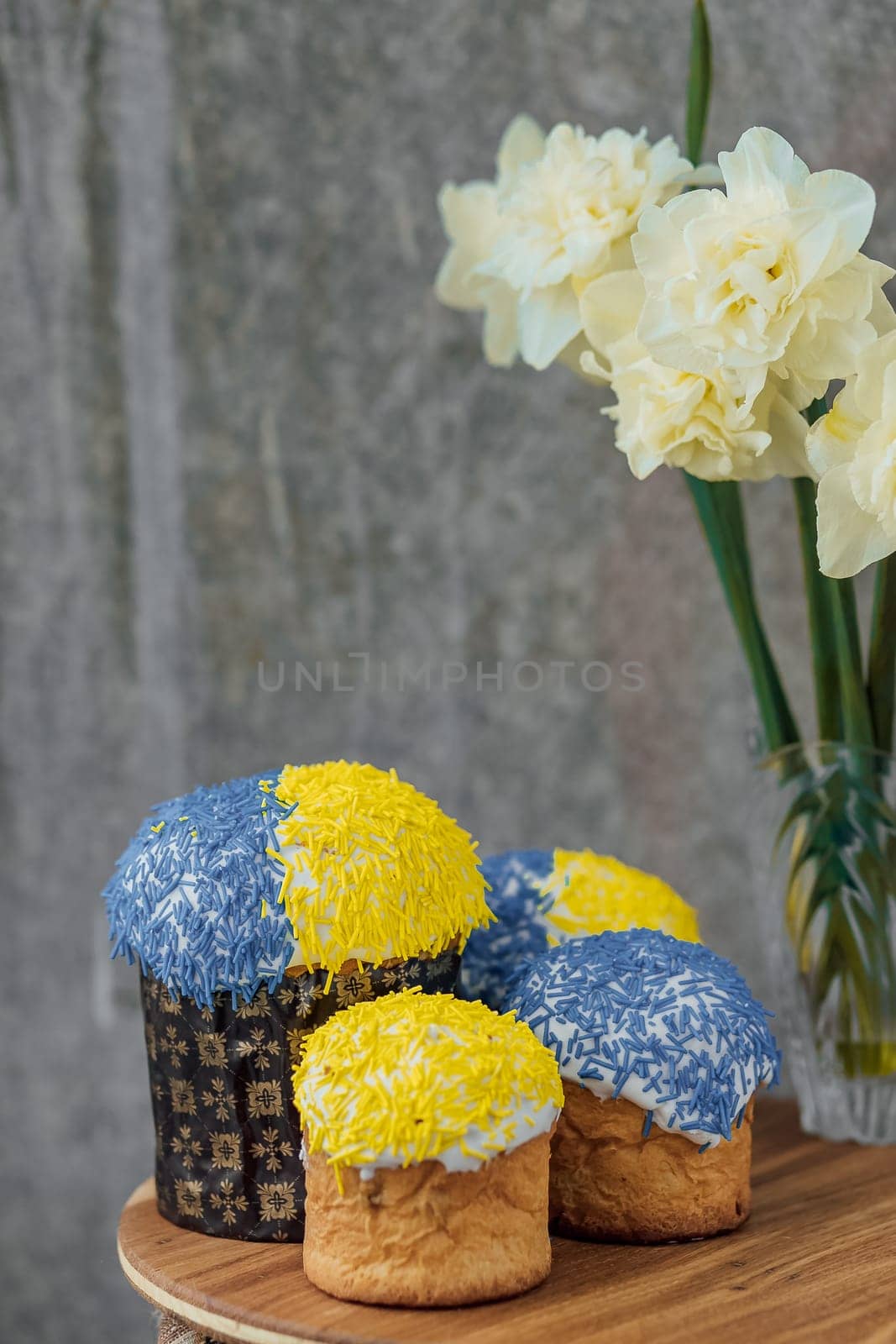 Delicious Easter cakes in the colors of the flag of Ukraine, yellow-blue colored Easter eggs on a wooden table with flowers in the background. place for text. selective focus by Anyatachka