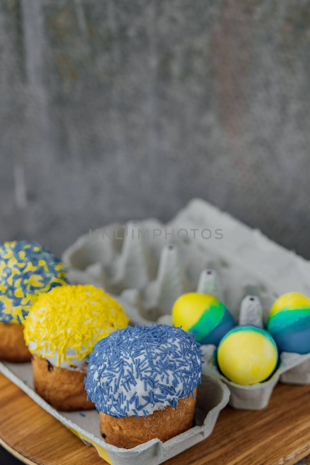 Easter cakes in the colors of the flag of Ukraine, yellow and blue in a cardboard stand with eggs, Easter eggs. place for text. selective focus by Anyatachka
