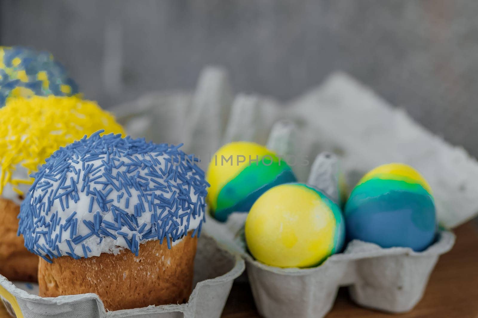 Easter cakes in the colors of the flag of Ukraine, yellow and blue in a cardboard stand with eggs, Easter eggs. place for text. selective focus.