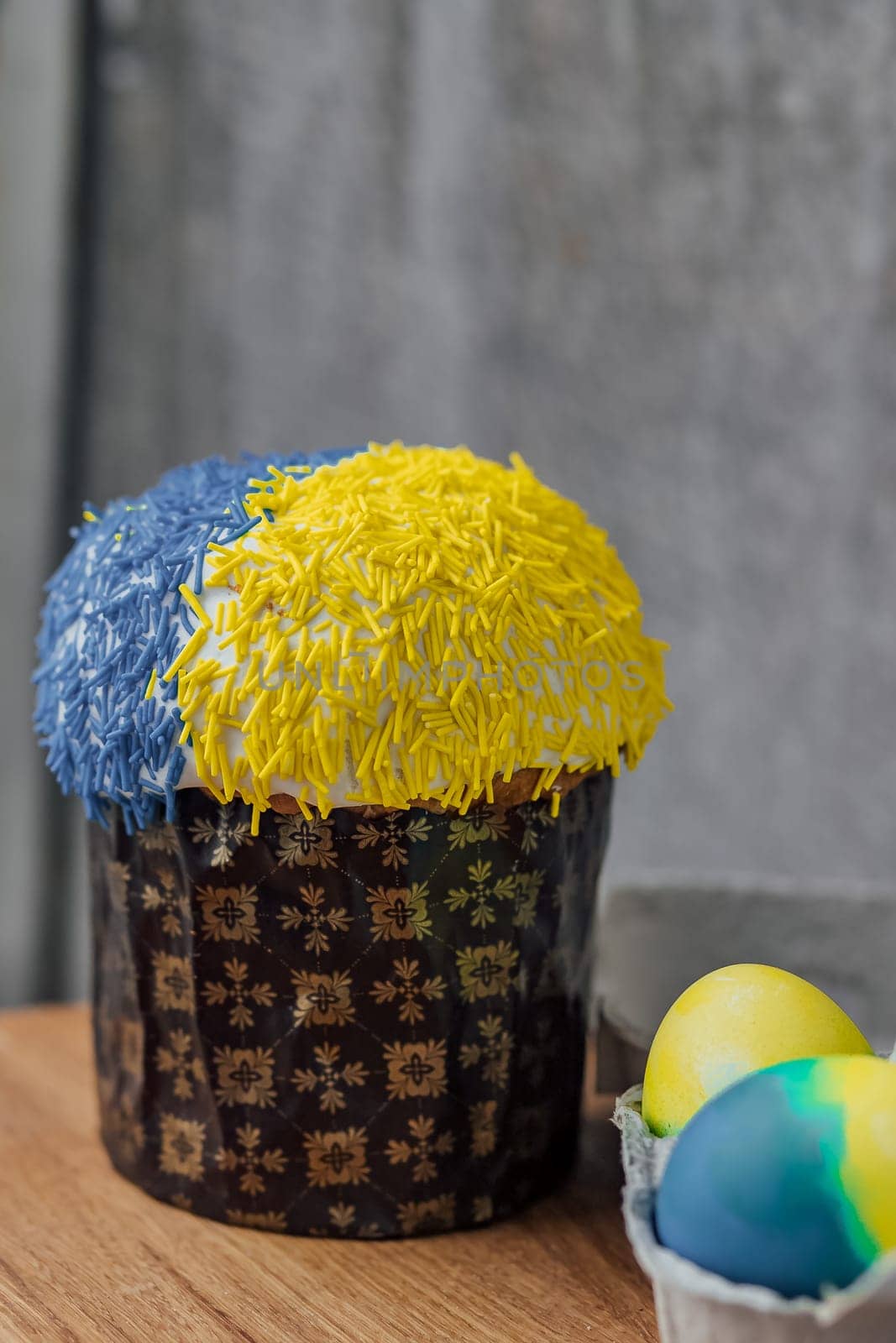 Easter cake is decorated with yellow-blue sprinkles on a gray background. place for text. patriotic paska in the color of the flag of Ukraine. Easter eggs.