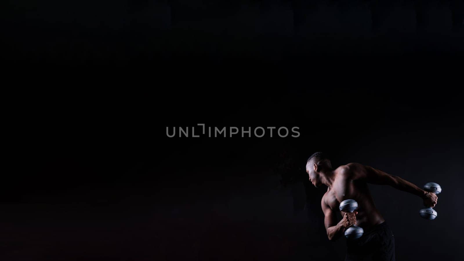 Isolated african muscular man with dumbbells on a dark studio background. Strong shirtless black guy