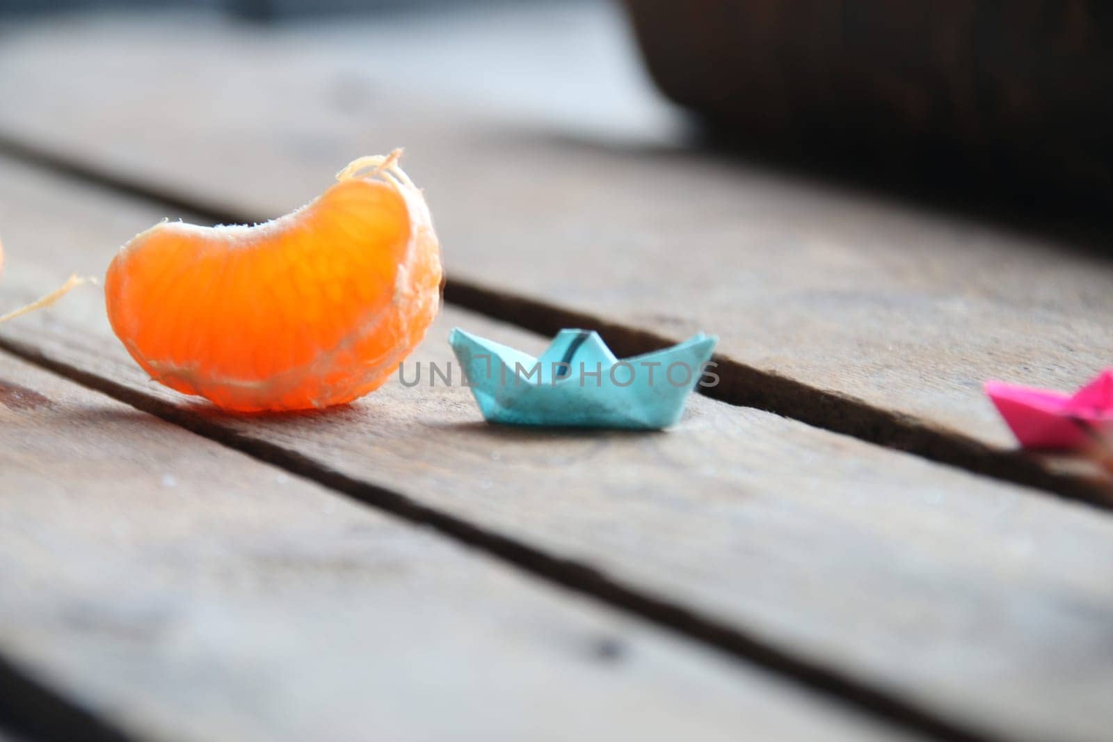 Slice of tangerine and paper and paper boat on vintage table. Summer time concept. by Markgraf