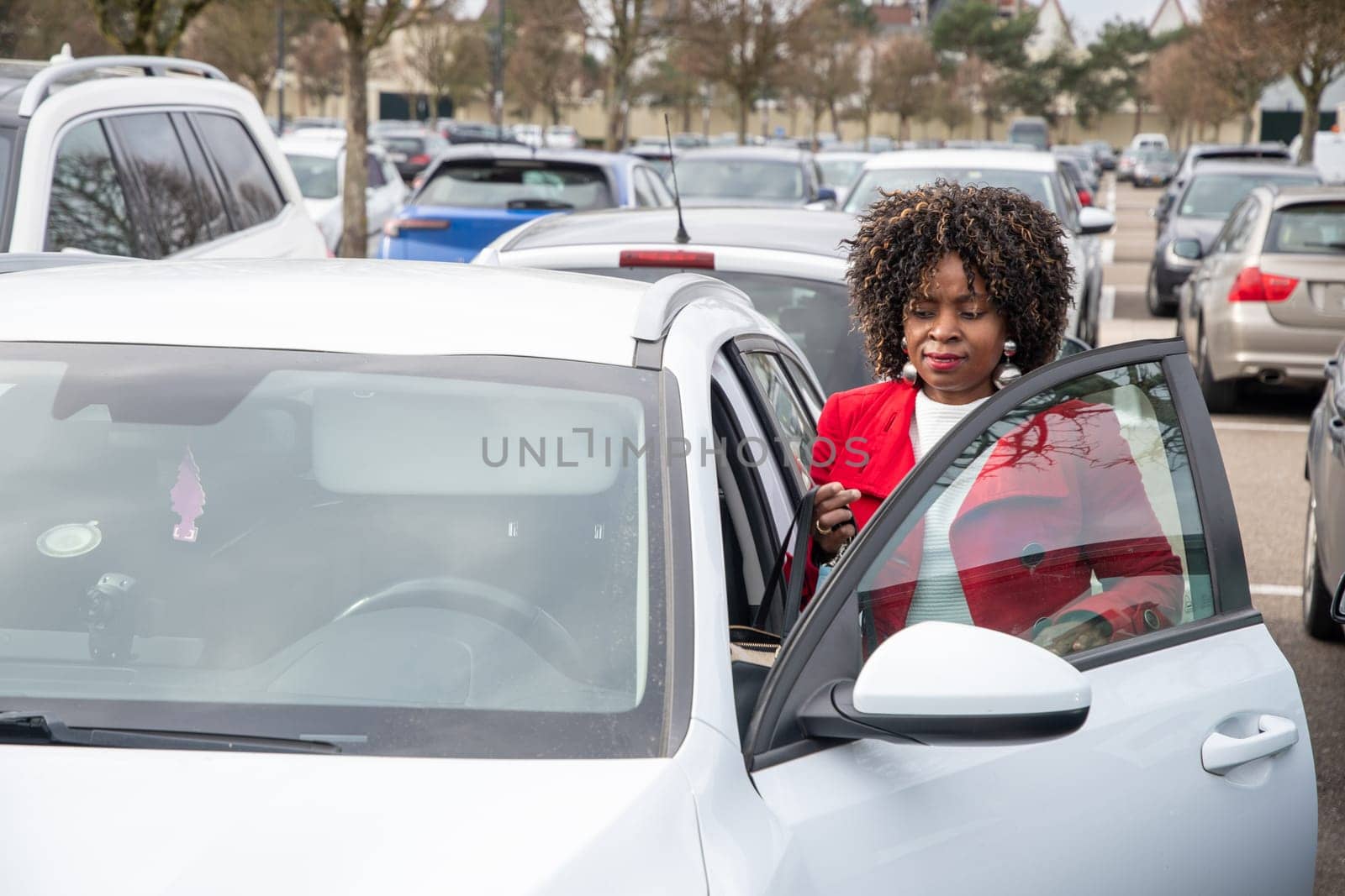 African American woman in a red coat opens the doors to get into a white car in a parking lot, personal transport, high quality photo
