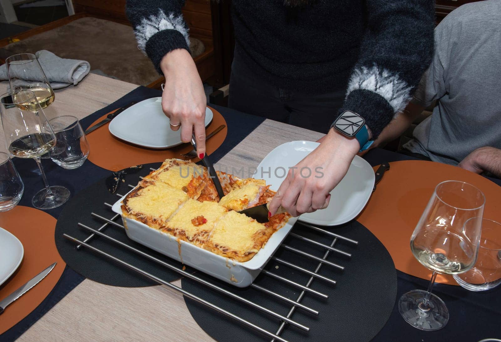 a woman serving hot homemade lasagna on plates to a family member sitting at the table, High quality photo