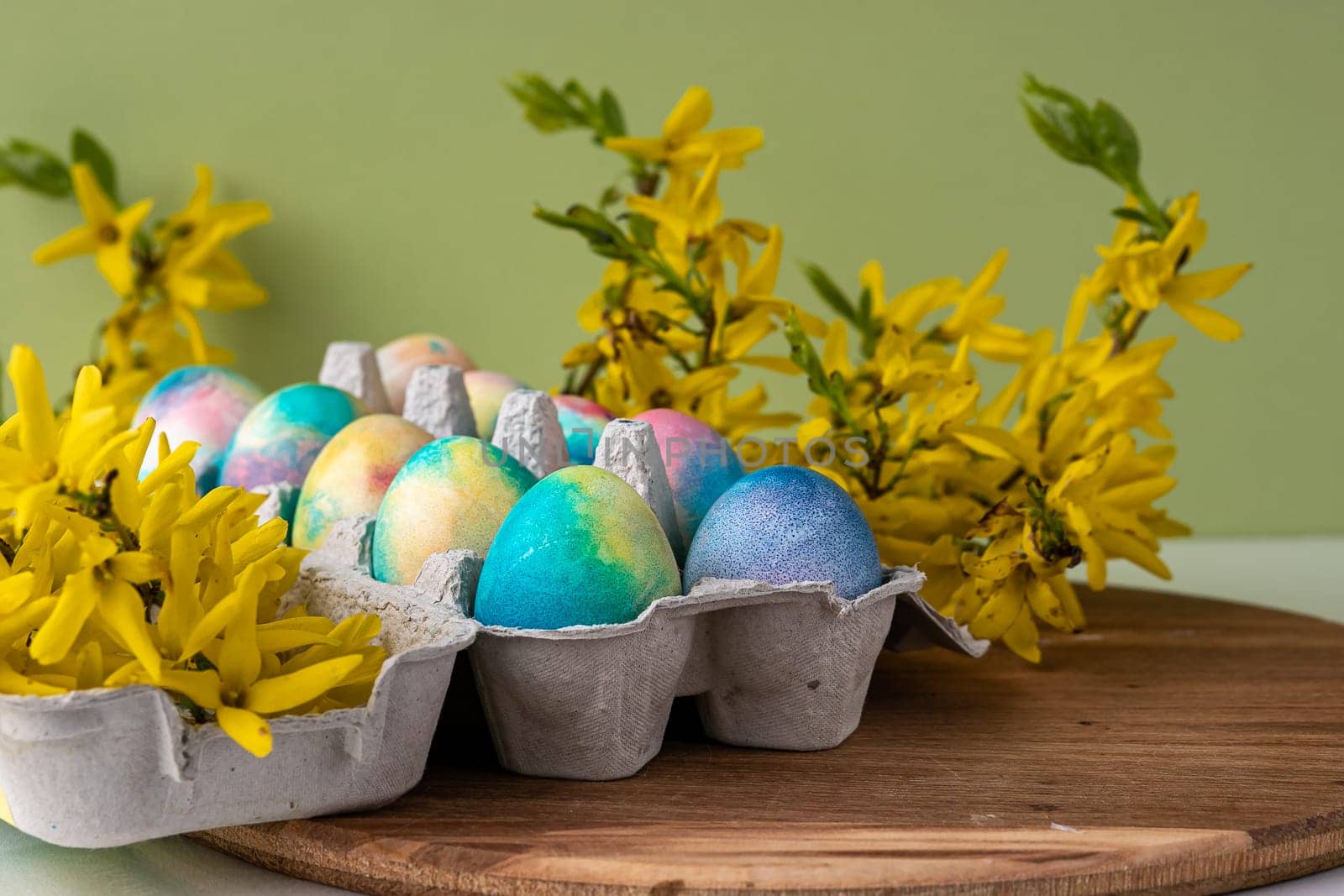 Happy Easter Easter eggs on rustic table with cherry blossoms. Natural dyed colorful eggs in paper tray on wooden board and spring flowers in rustic room. Moody atmospheric image