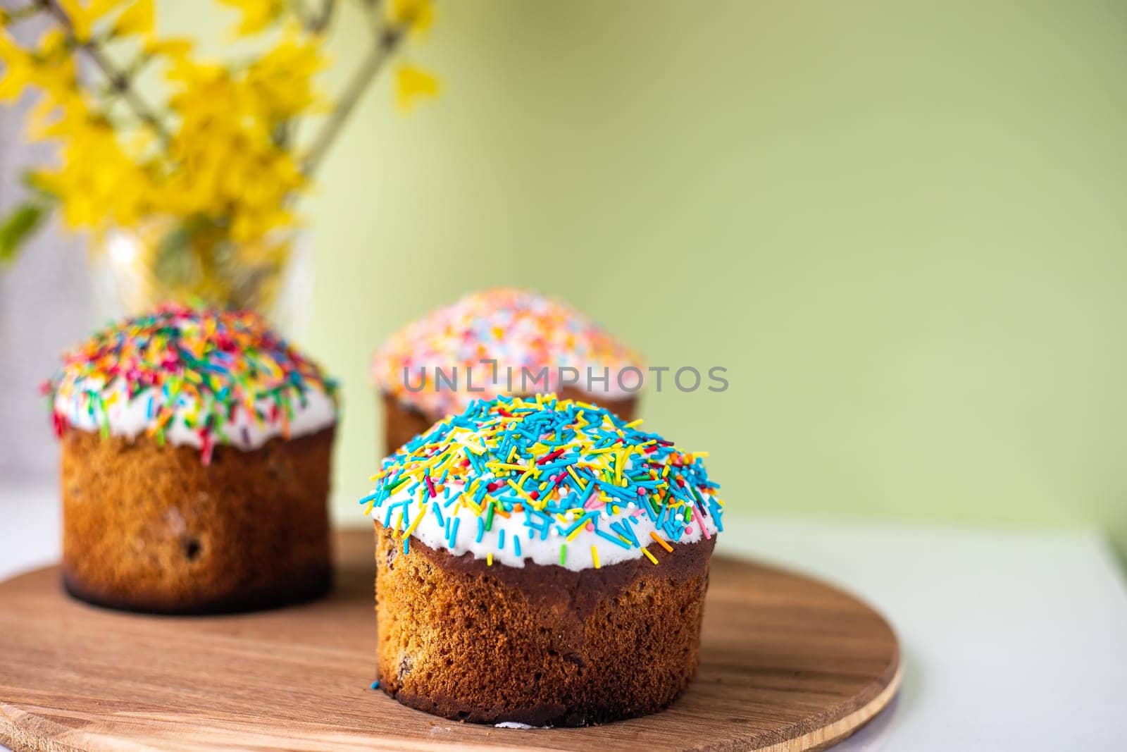 Easter composition with Easter cakes, wooden stand and spring flowers on a yellow background. copy space.
