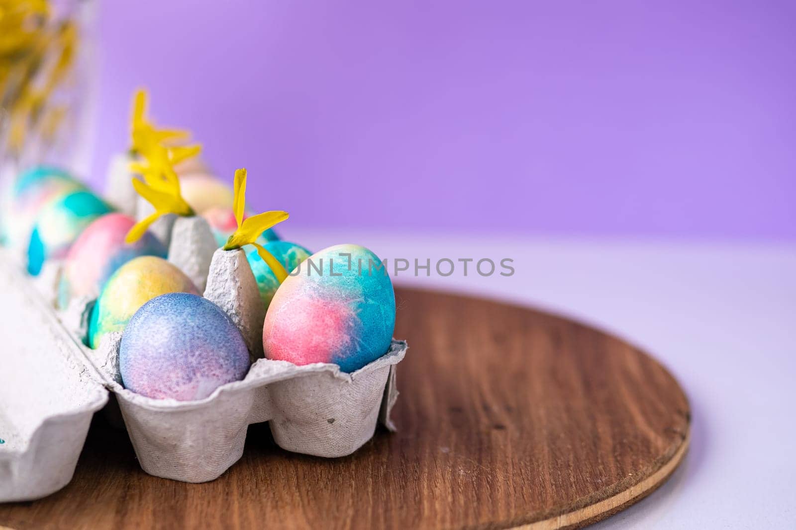 Easter composition with colorful eggs in a basket, spring yellow flowers on a purple background. Banner. Copy space. by Anyatachka