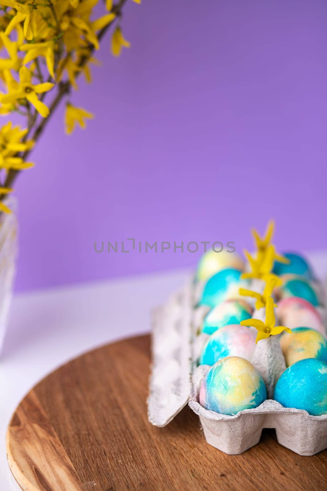 Easter composition with colorful eggs in a basket, spring yellow flowers on a purple background. Banner. Copy space