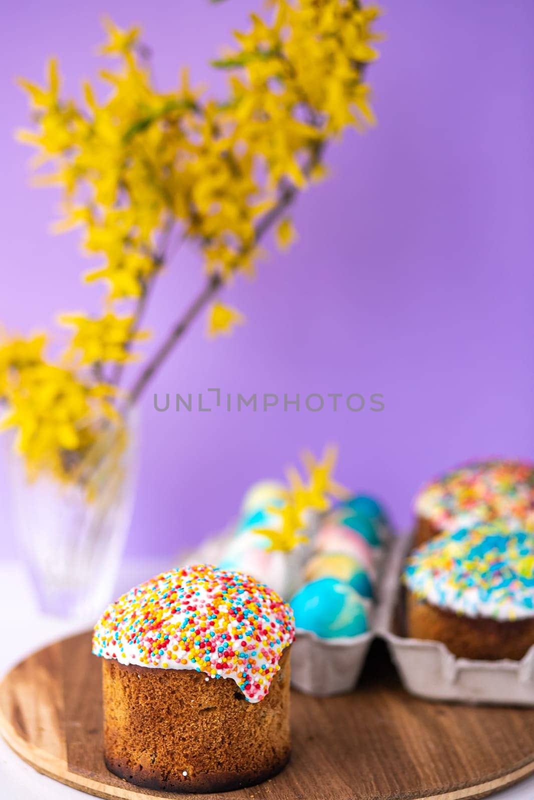 Easter cake on a purple background with yellow spring flowers. easter colored eggs. Easter food. minimal concept