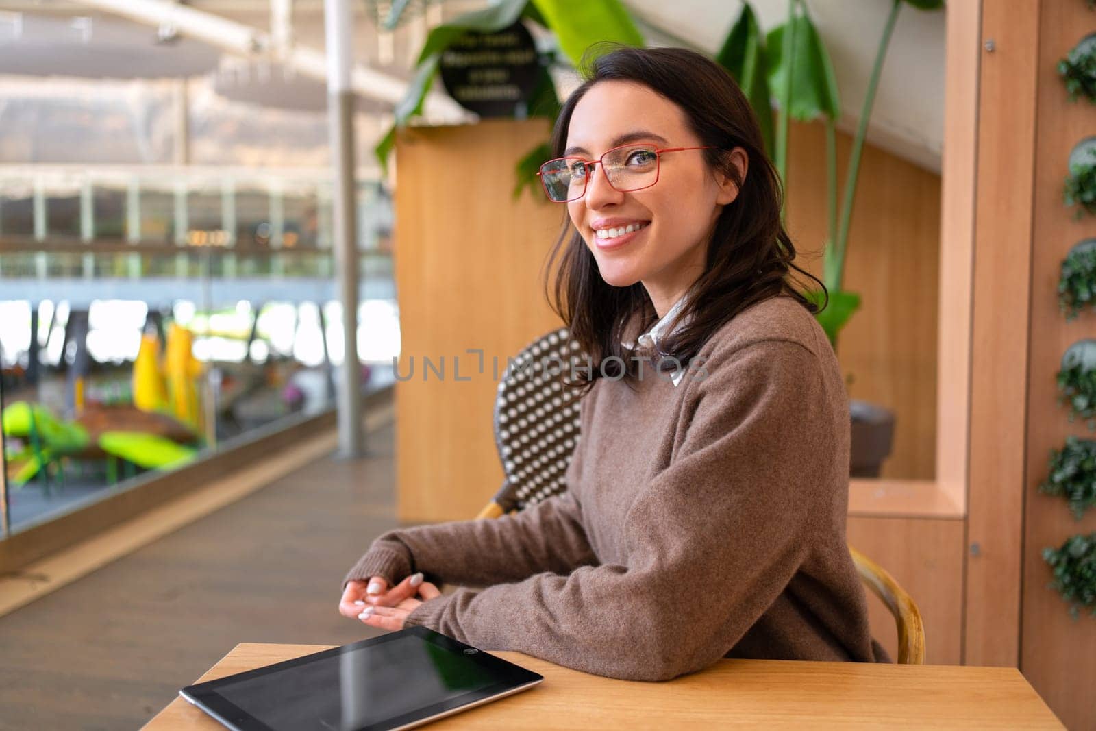 Woman student with tablet computer sitting at her desk smile and looking away. Female person studying or working online on touch pad. Modern technologies and communication.