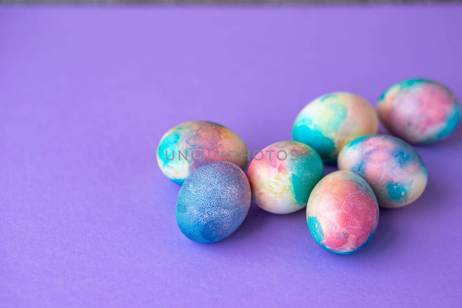 Easter composition with colorful eggs in shopping cart, wooden bunny and spring flowers on purple background. Easter frame of eggs painted in purple color. Copy space.