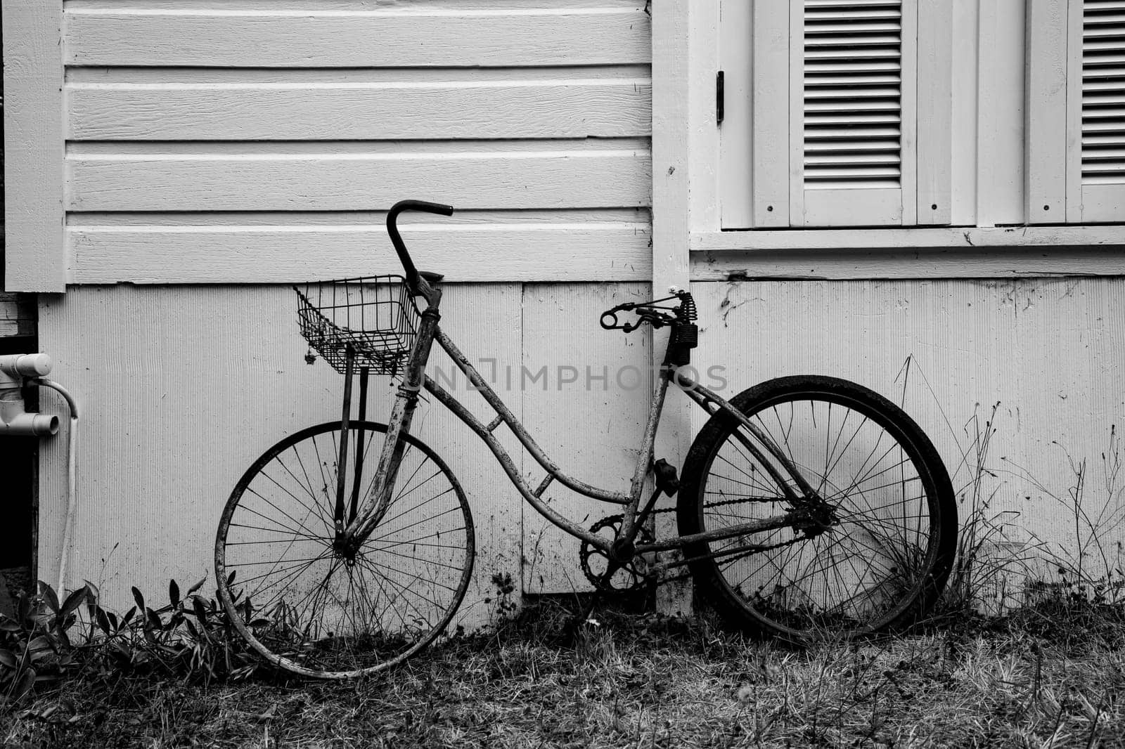 An old bicycle leaning against a house with a metal basket on the front in black and white by Granchinho