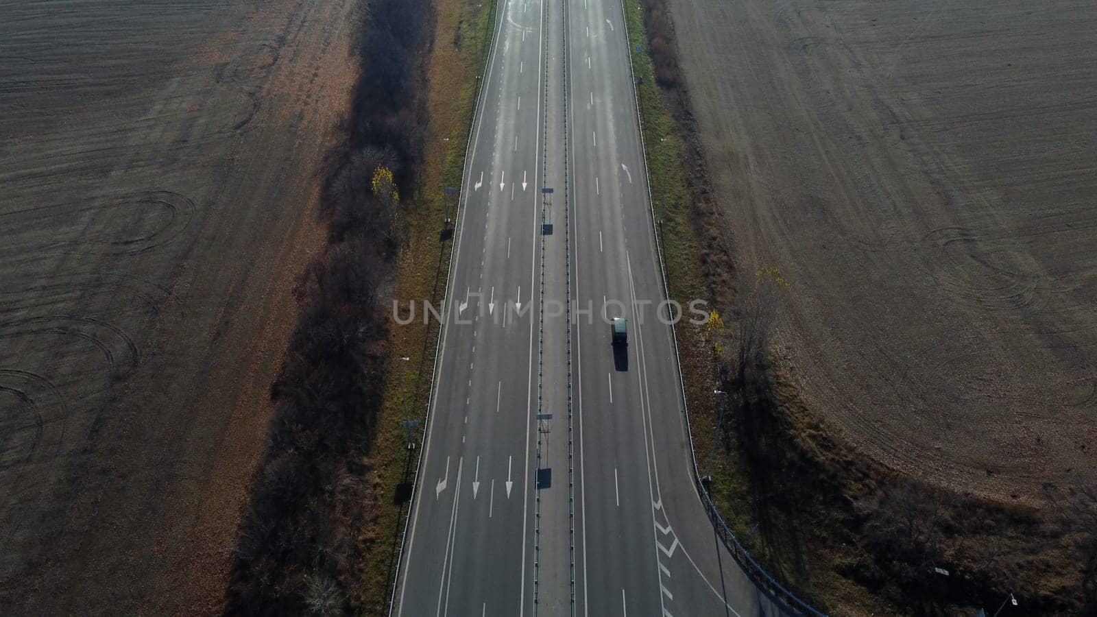 Cars driving along the highway on an autumn sunny day. Automobile road with white markings between agricultural fields. View of the cars driving on paved road. automobile vehicles. Aerial drone view.