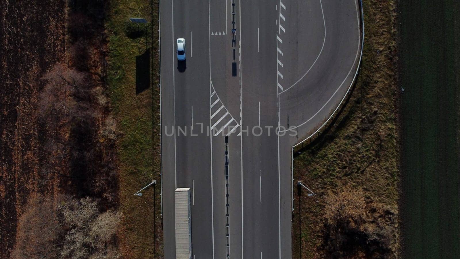 Cars driving along highway on autumn sunny day. Automobile road with white markings between agricultural fields. View of cars driving on paved road. Automobile vehicles. Top view. Aerial drone view.