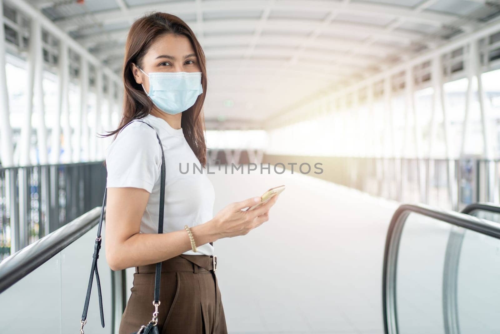 Portrait of a young woman in a medical mask for anti-coronavirus COVID-19 pandemic infectious disease outbreak protection and use a smartphone in Public area. Concept of Virus pandemic and pollution by PattyPhoto