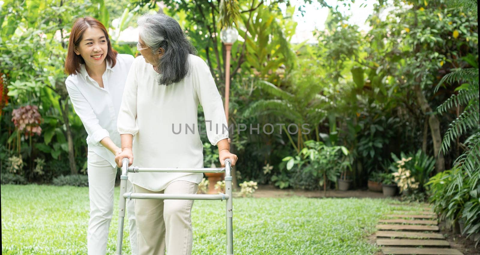 An old elderly Asian woman uses a walker and walking in the backyard with her daughter.  Concept of happy retirement With care from a caregiver and Savings and senior health insurance