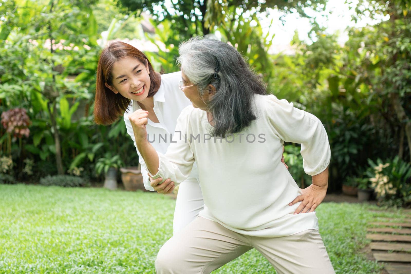 An old elderly Asian woman and exercise in the backyard with her daughter.  Concept of happy retirement With care from a caregiver and Savings and senior health insurance, Happy family by PattyPhoto