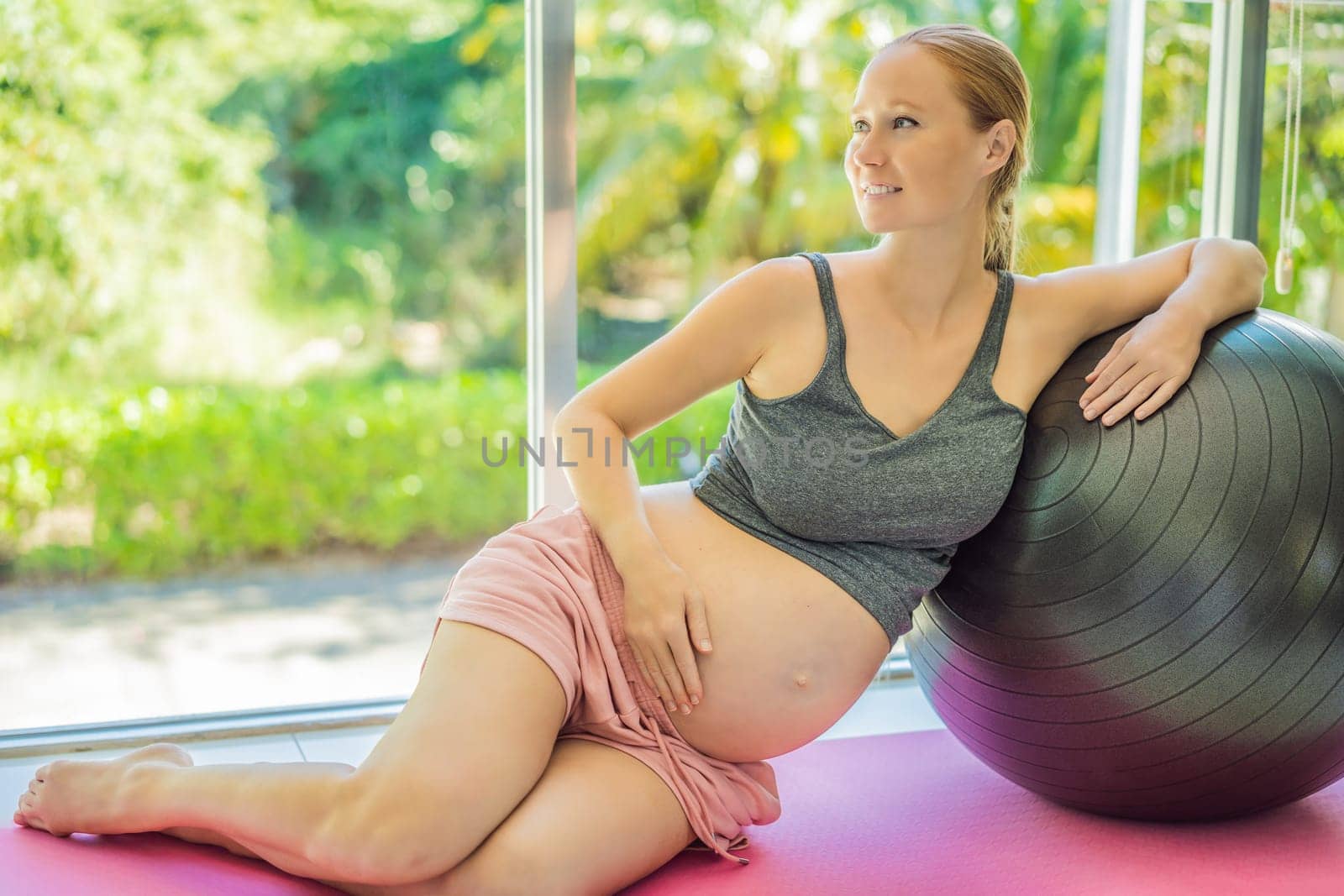 Pregnant woman exercising on fitball at home. Pregnant woman doing relax exercises with a fitness pilates ball. Against the background of the window.