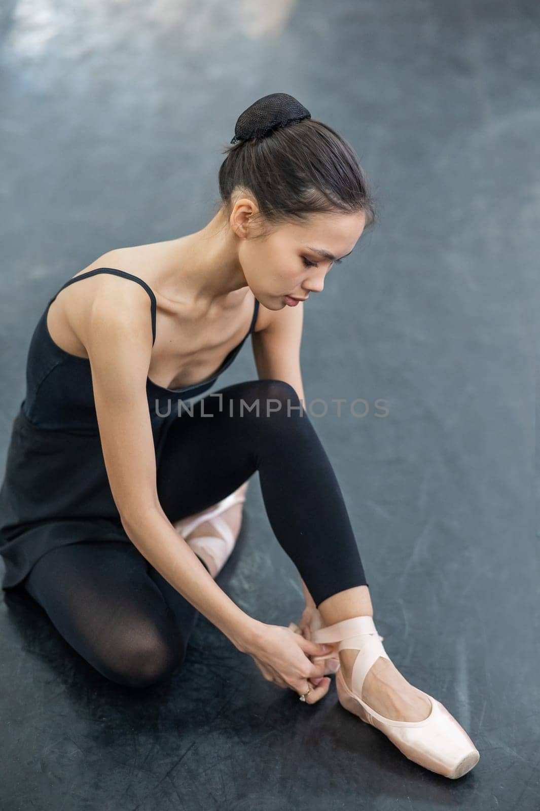 Asian woman puts on pointe shoes by tying ribbons on her ankle