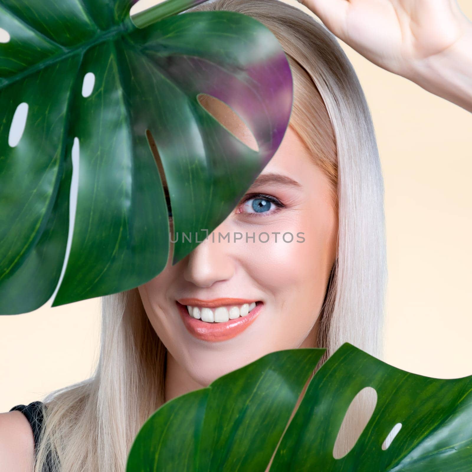 Closeup facial portrait personable woman with perfect smooth makeup holding green monstera leaves and cover her face as natural healthy skincare treatment. Tropical nature and beauty concept