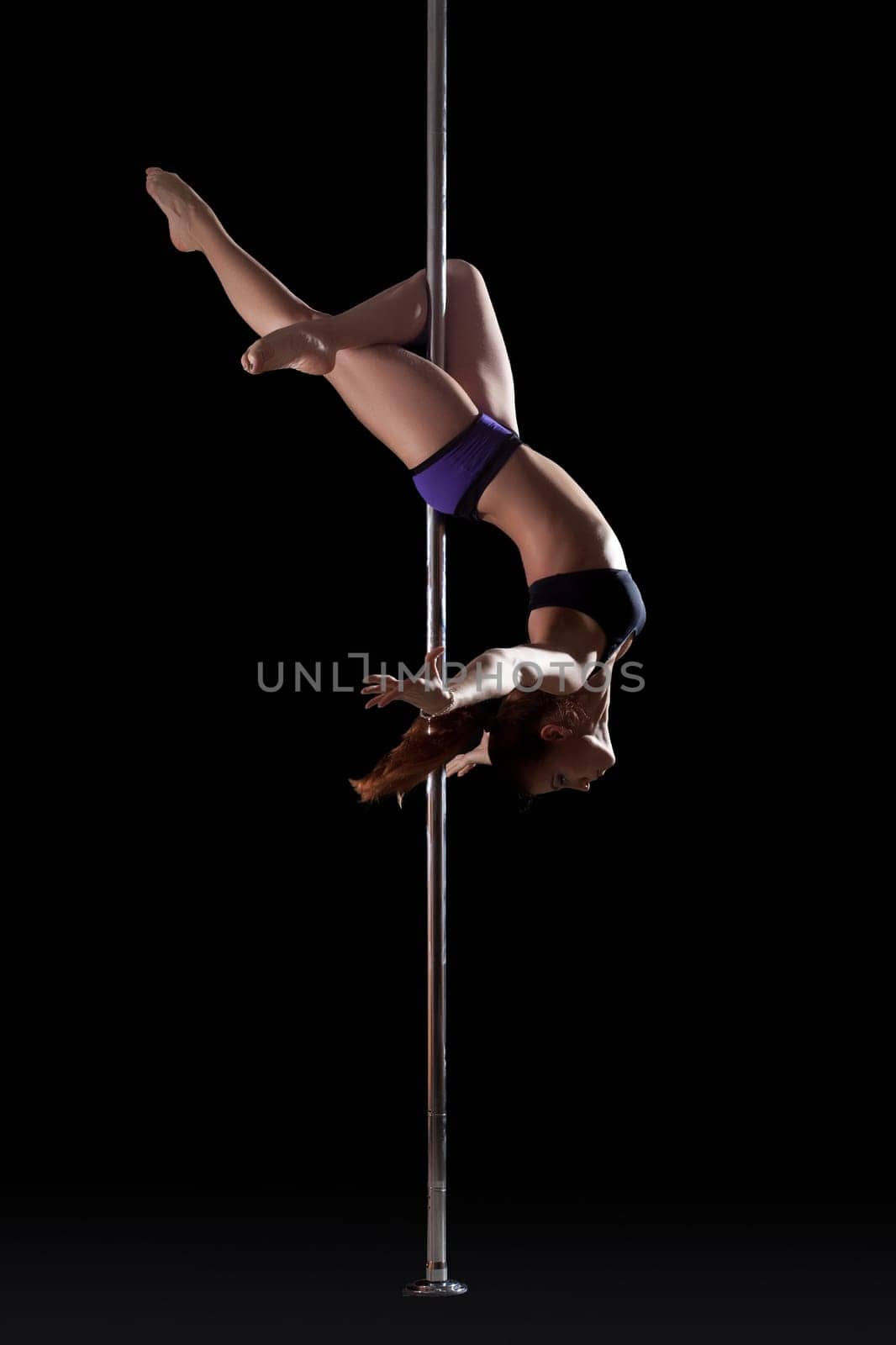 Athletic young pole dancer, isolated on black background