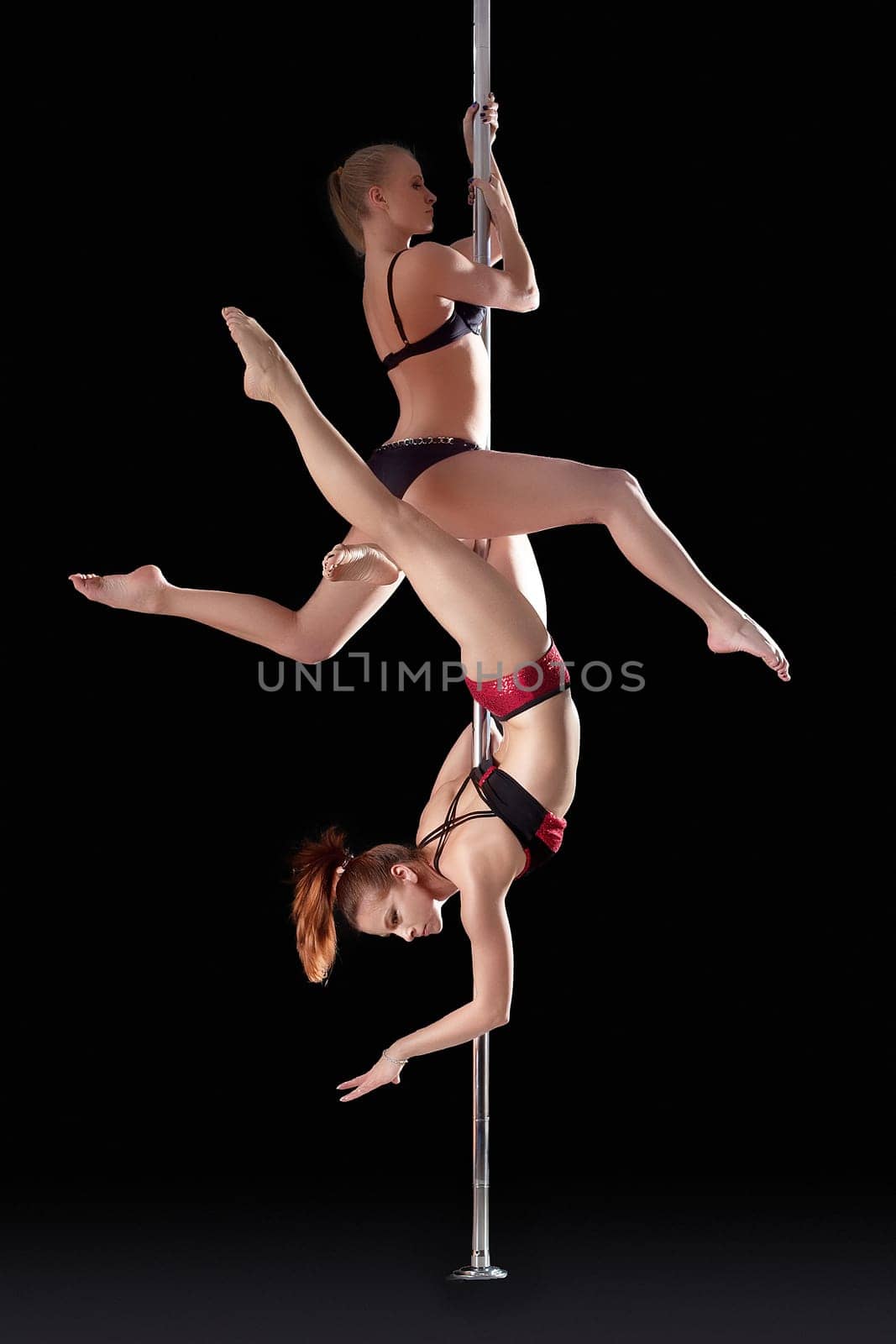 Two athletic young girls dancing on pilon, isolated over black