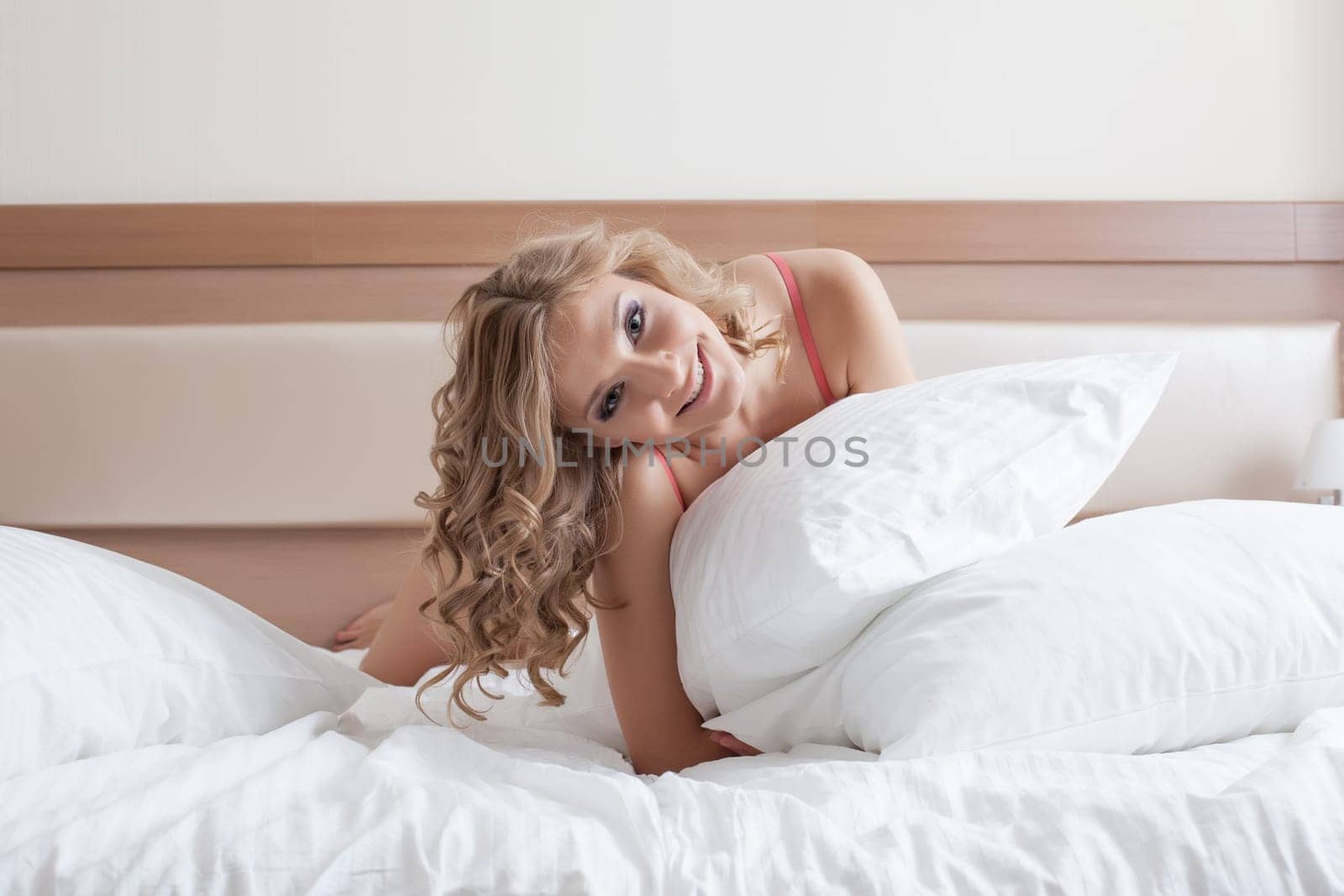 Image of smiling curly blonde posing with pillow, close-up