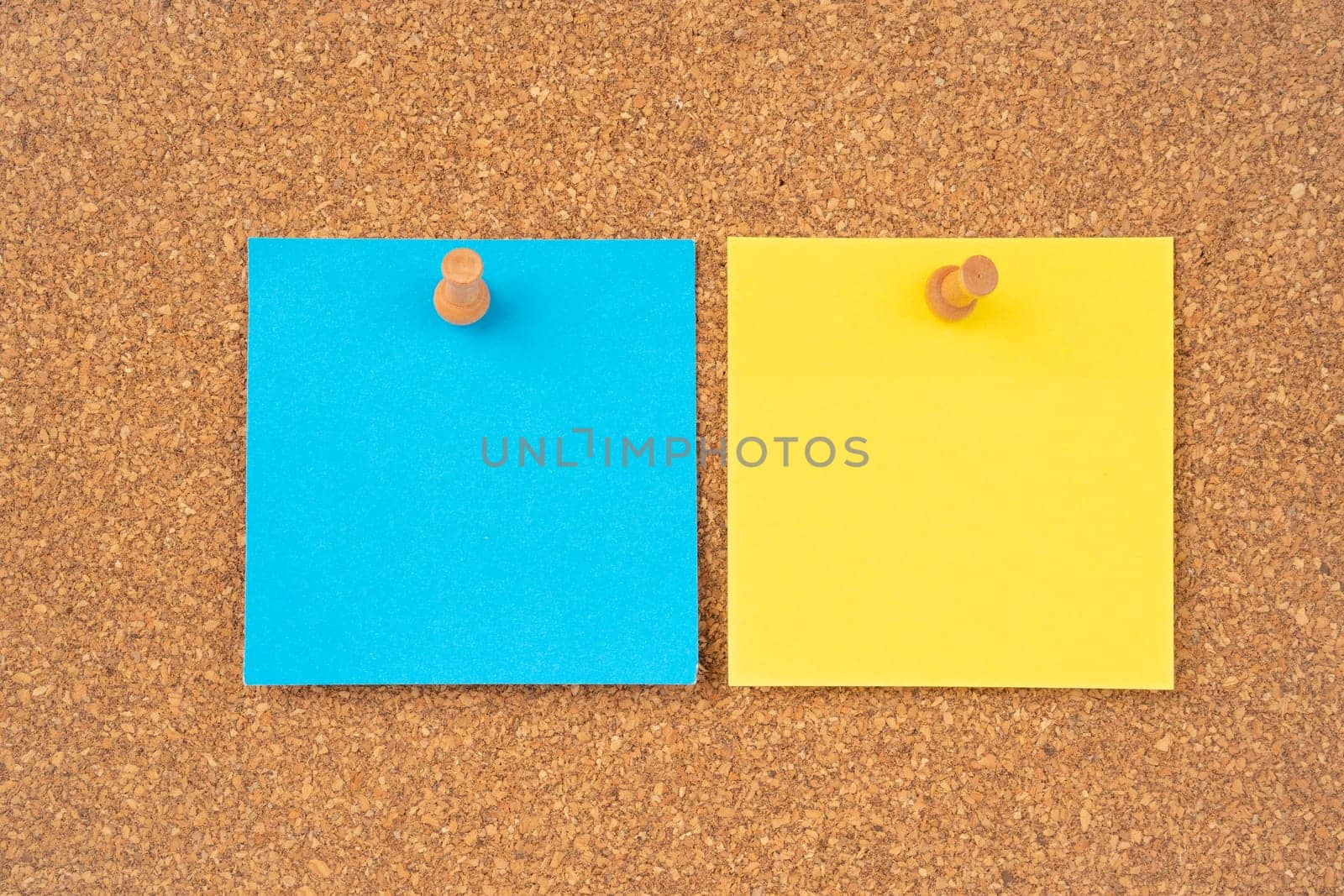 Blank yellow and blue color sticky note paper and wooden thumbtack on wooden background.