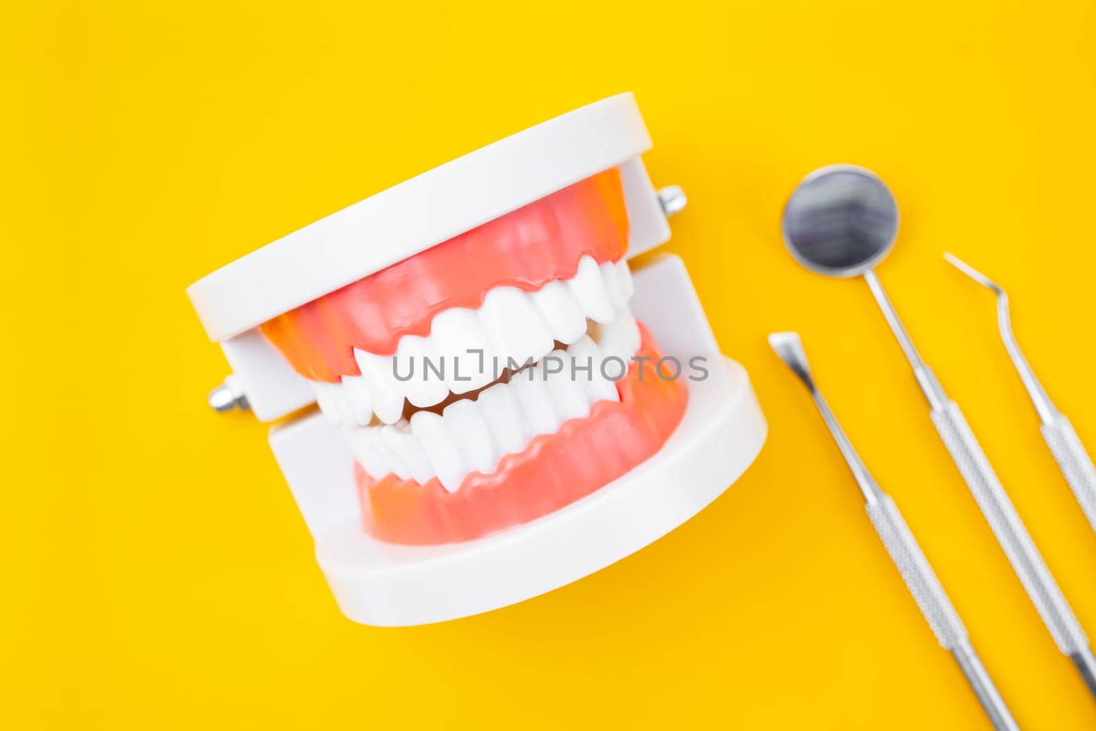 The Dentures model and instrument dental on yellow background. by Gamjai