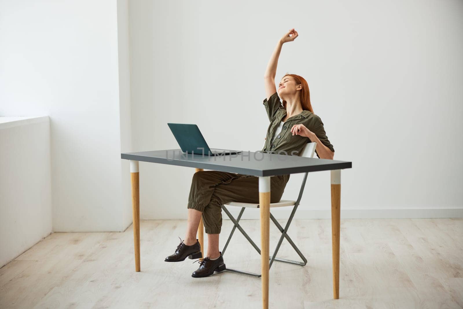 a very happy woman sits at a laptop and rejoices at the completed tasks raising her hands up. High quality photo