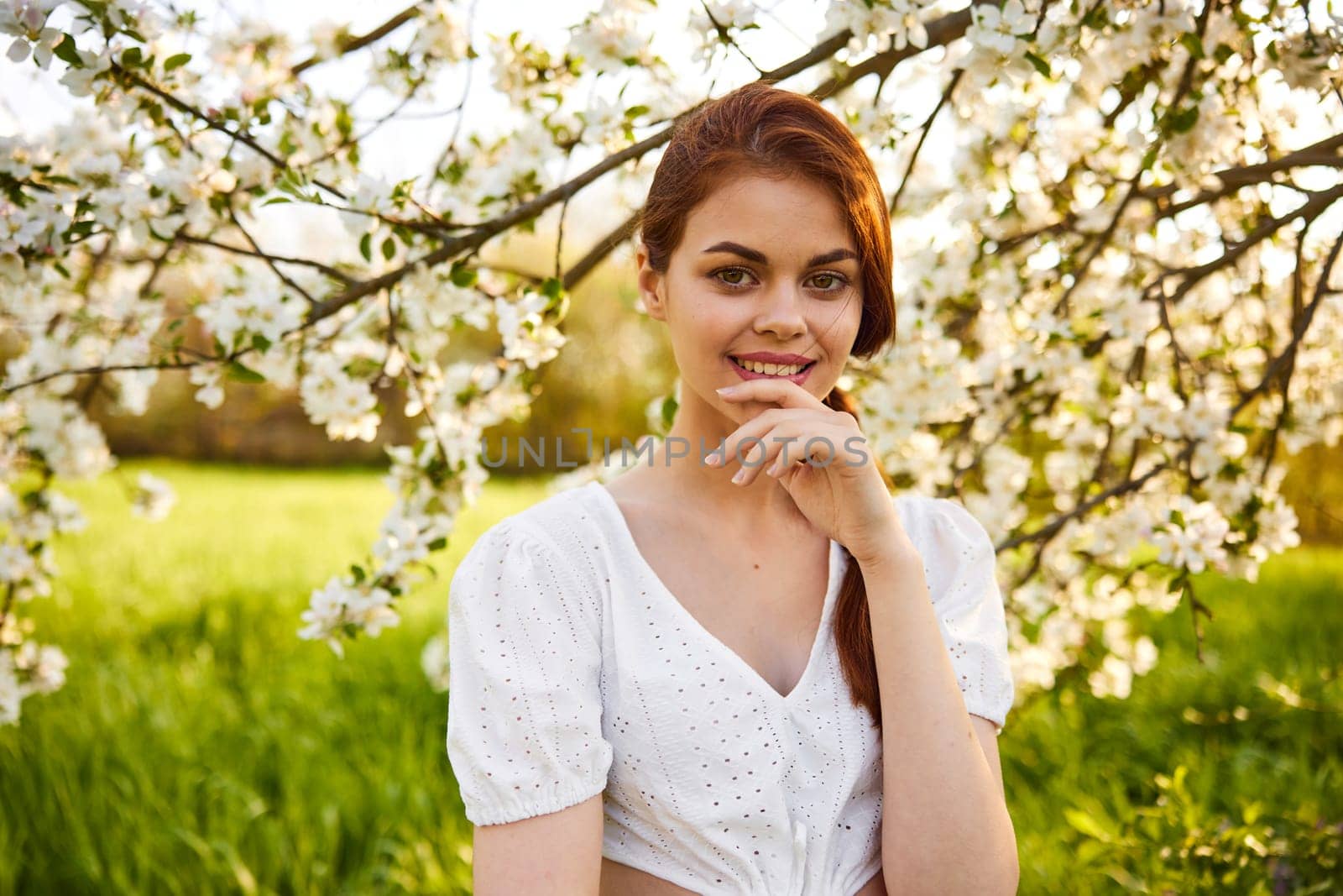 portrait of beautiful young woman standing near the apple tree on a warm summer sunny day against sun light sky background Copy space for inscription by Vichizh