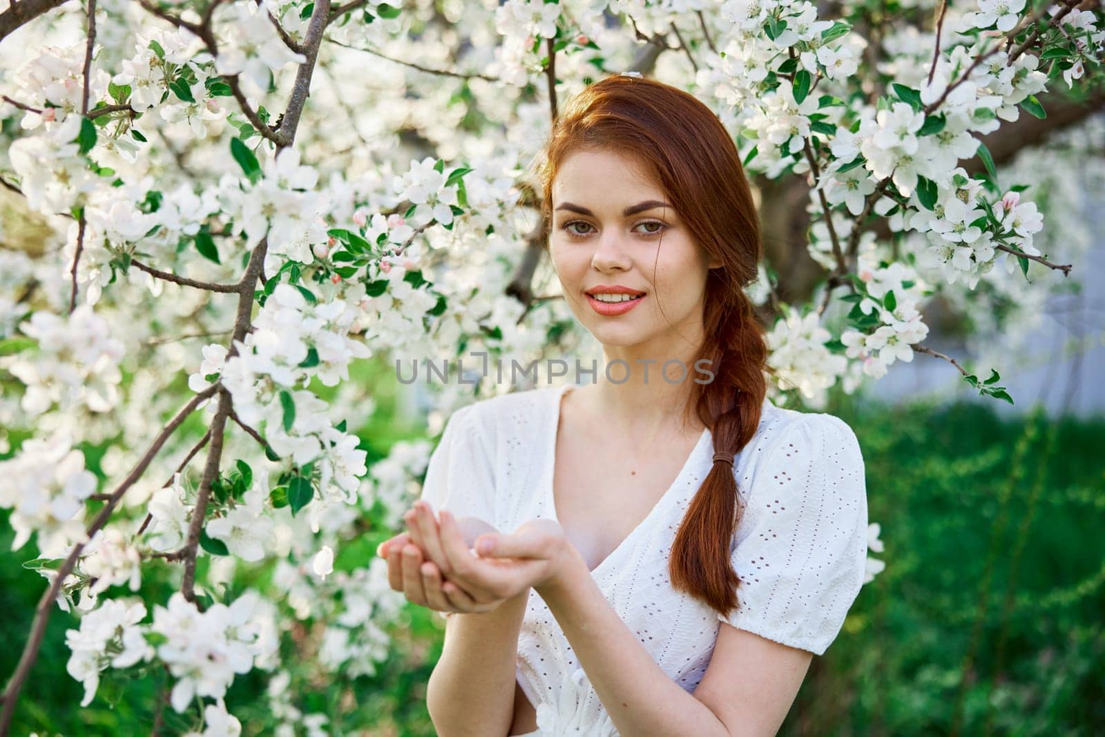 portrait of a beautiful red-haired woman against the background of a flowering tree with flowers in her palms by Vichizh