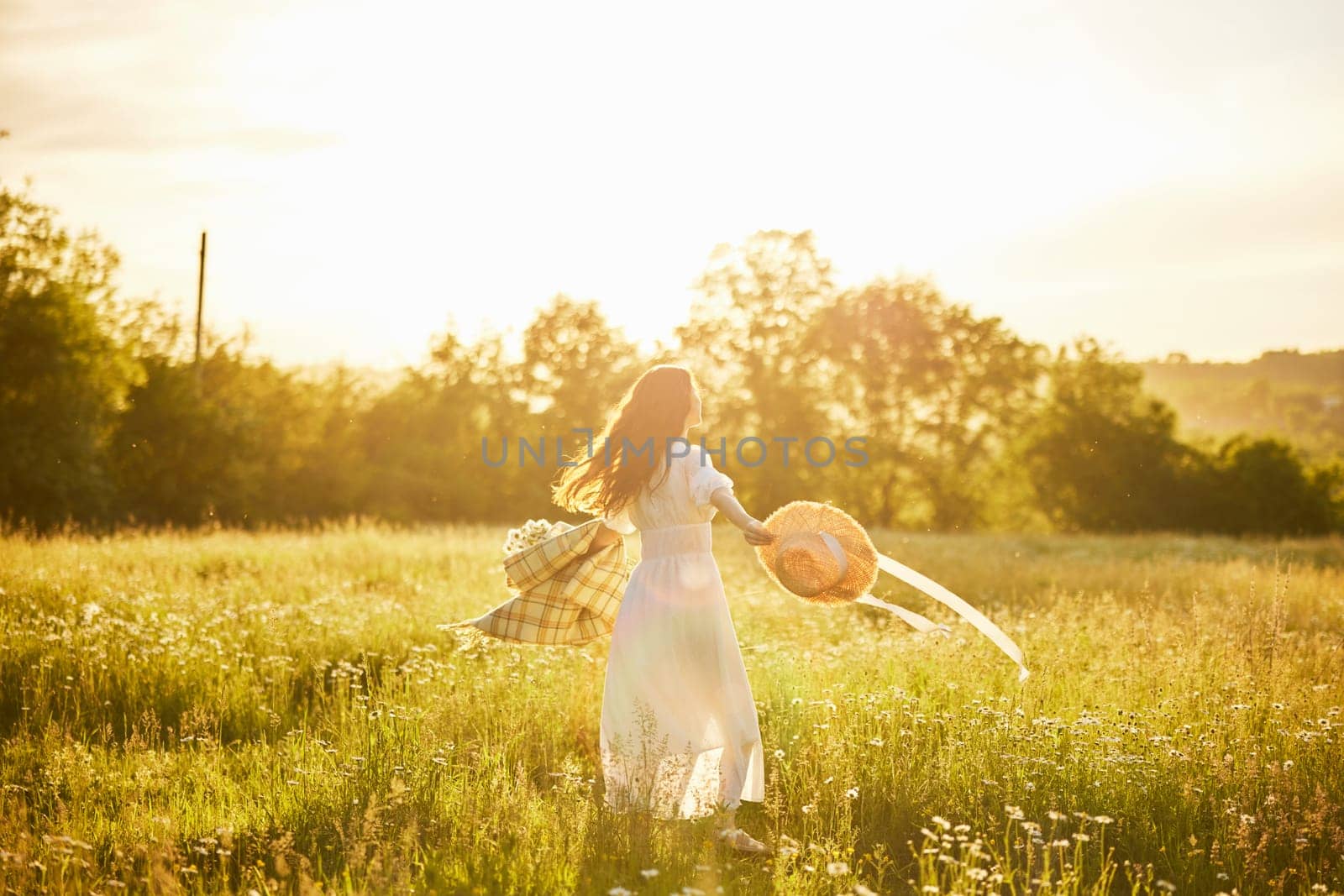 a woman in a light dress with a hat in her hands is spinning in nature in the rays of the setting sun. High quality photo