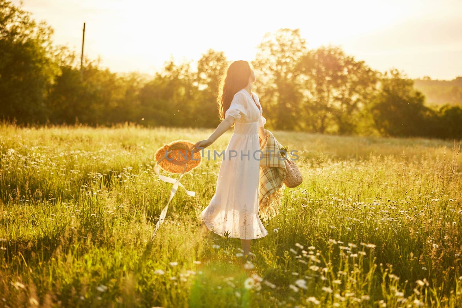 a woman in a light dress with a hat in her hands is spinning in nature in the rays of the setting sun. High quality photo