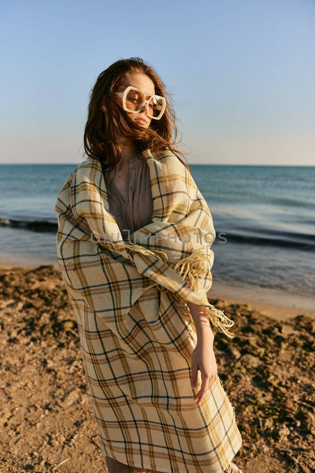 cute woman stands with a plaid during sunset on the beach. Rest, enjoyment. High quality photo