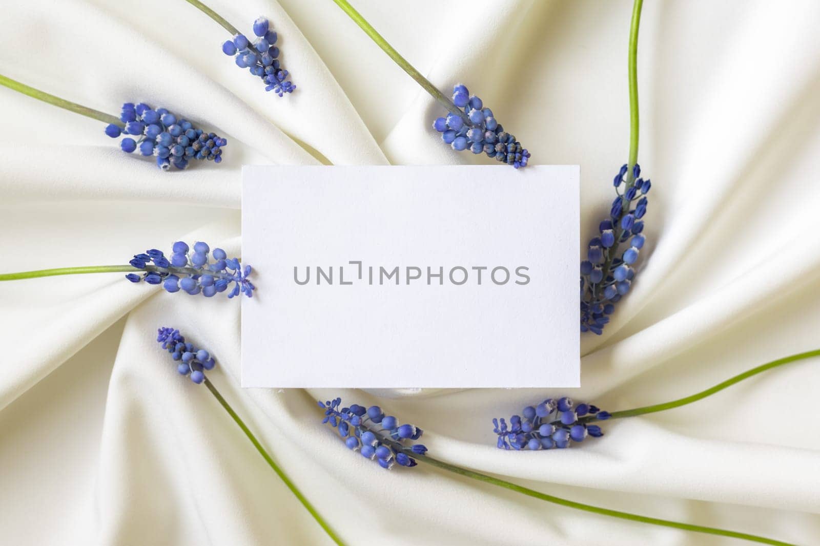 Paper blank in frame of blue spring flowers. Flat lay. Close-up. Copy space for inspirational texts, beautiful quotes or positive sayings