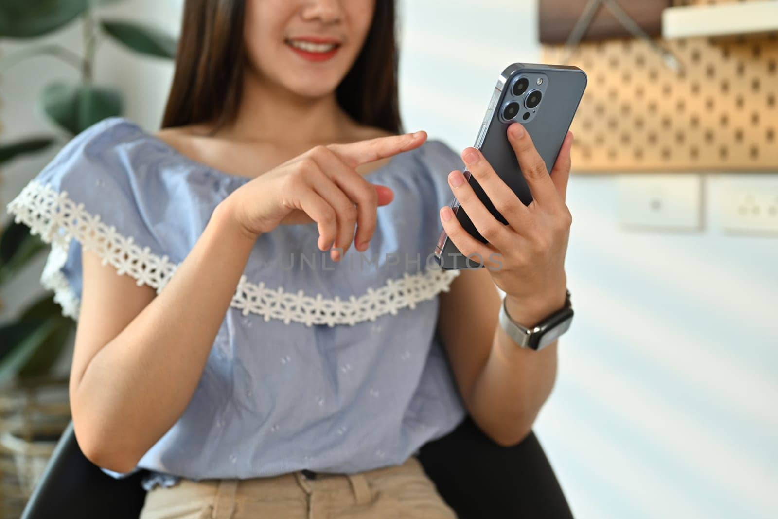 Smiling young adult asian woman chatting with client online on smart phone and using laptop at her workplace by prathanchorruangsak