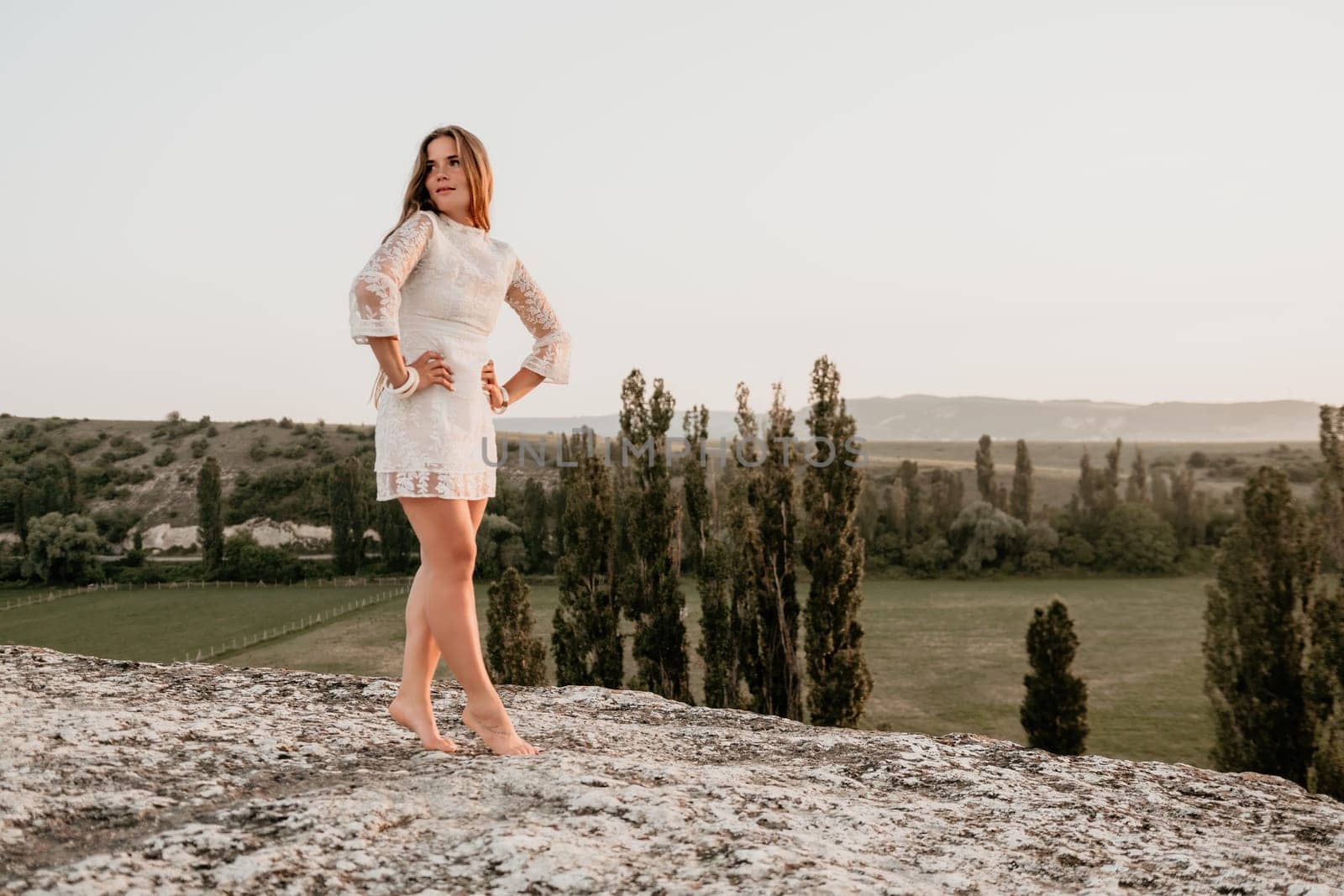 Romantic beautiful bride in white dress posing with sea and mountains in background. Stylish bride standing back on beautiful landscape of sea and mountains on sunset