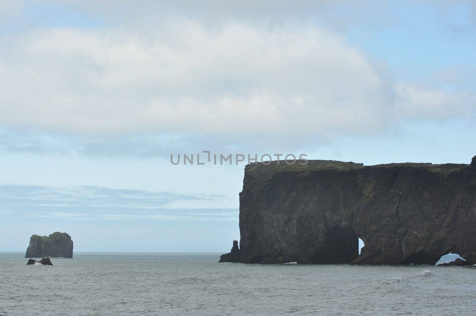 Scenic view of Icelandic peninsula with waves hitting huge black rocks at overcast Dyrholaey Cape