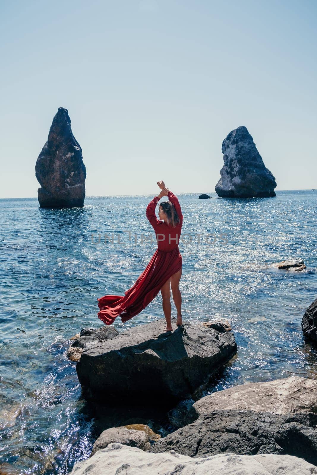 Woman travel sea. Young Happy woman in a long red dress posing on a beach near the sea on background of volcanic rocks, like in Iceland, sharing travel adventure journey