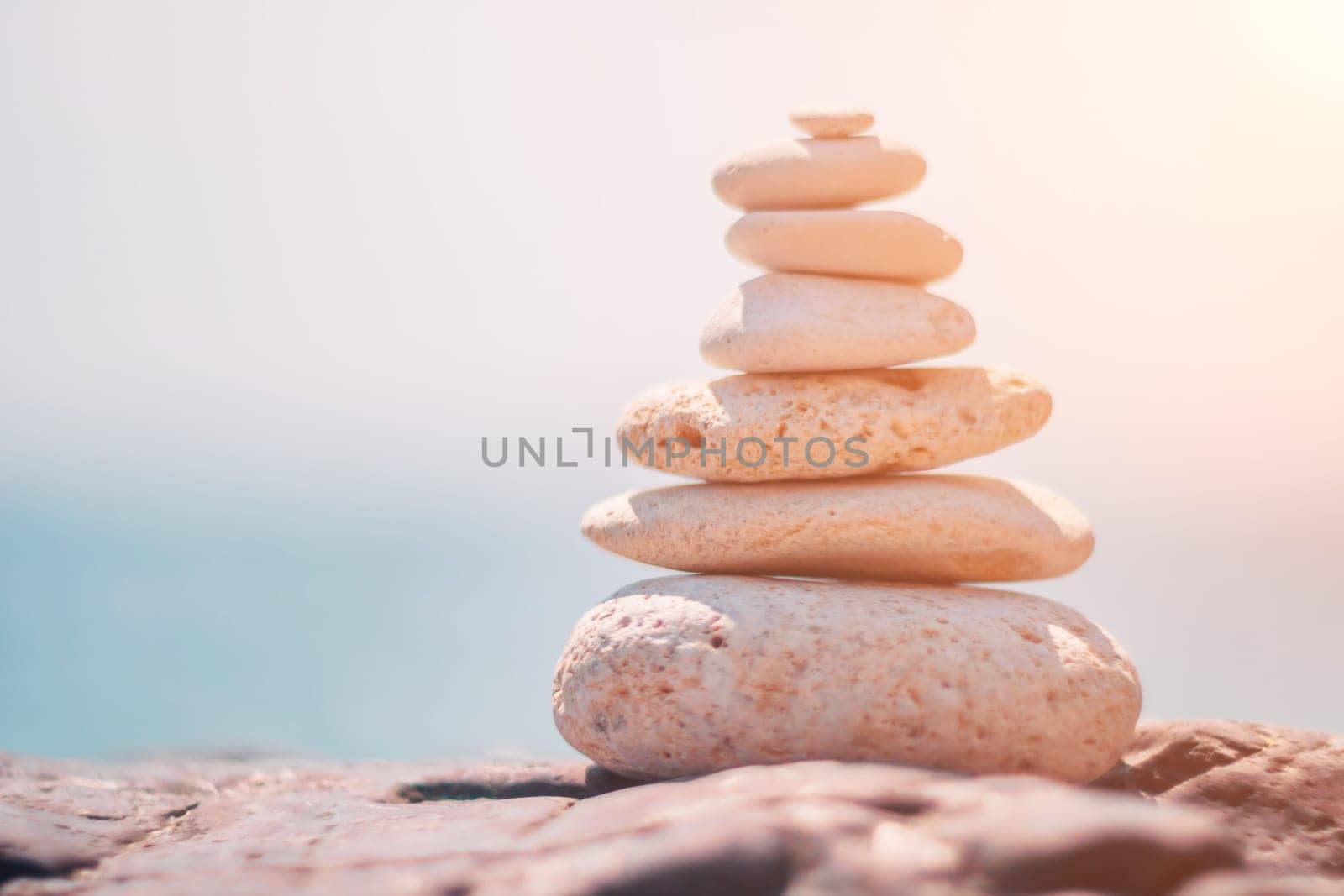 Balanced rock pyramid on sea pebbles beach, sunny day and clear sky at sunset. Golden sea bokeh on background. Selective focus, zen stones on sea beach, meditation, spa, harmony, calm, balance concept by panophotograph