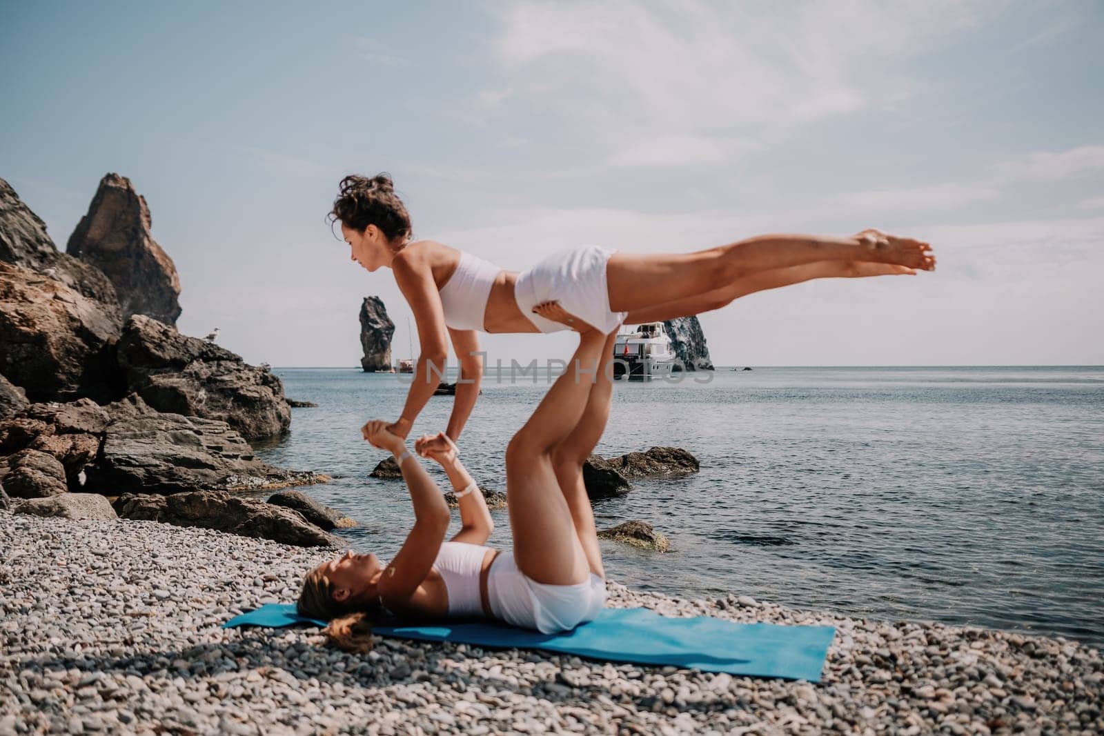 Woman sea yoga. Two Happy women meditating in yoga pose on the beach, ocean and rock mountains. Motivation and inspirational fit and exercising. Healthy lifestyle outdoors in nature, fitness concept. by panophotograph