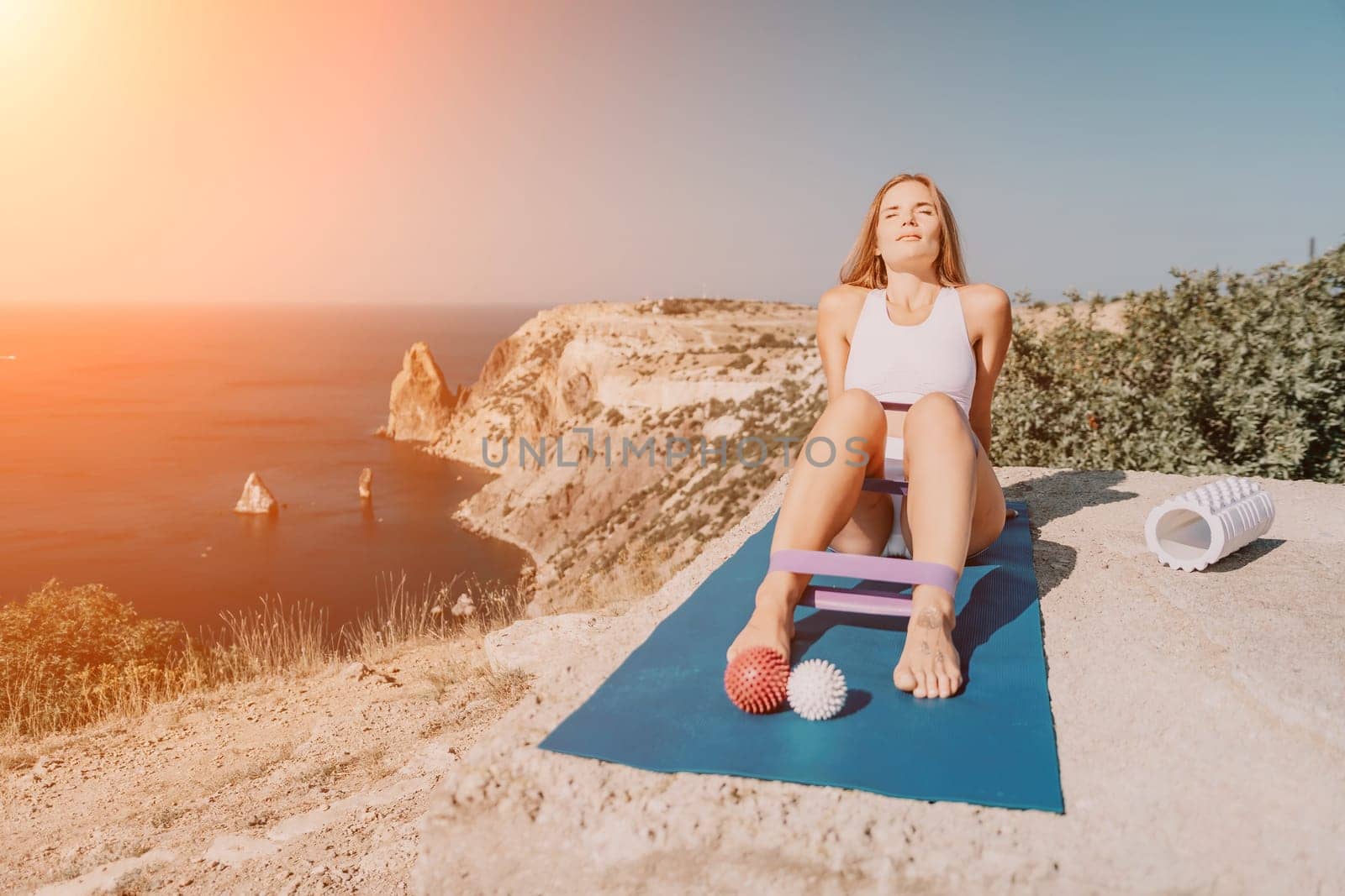 Middle aged well looking woman with black hair doing Pilates with the ring on the yoga mat near the sea on the pebble beach. Female fitness yoga concept. Healthy lifestyle, harmony and meditation.