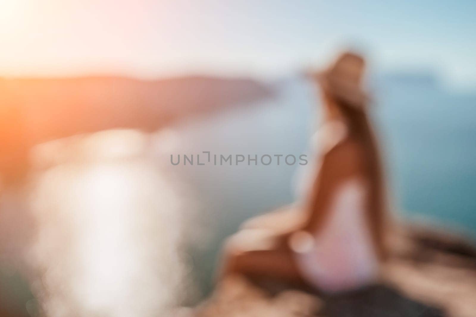 Abstract defocused digital nomad, woman in the hat, a business woman with a laptop sits on the rocks by the sea during sunset. Freelance, remote work on vacation. by panophotograph