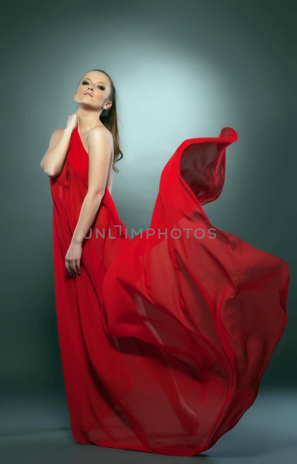 Graceful naked girl posing in red flying cloth, on gray background