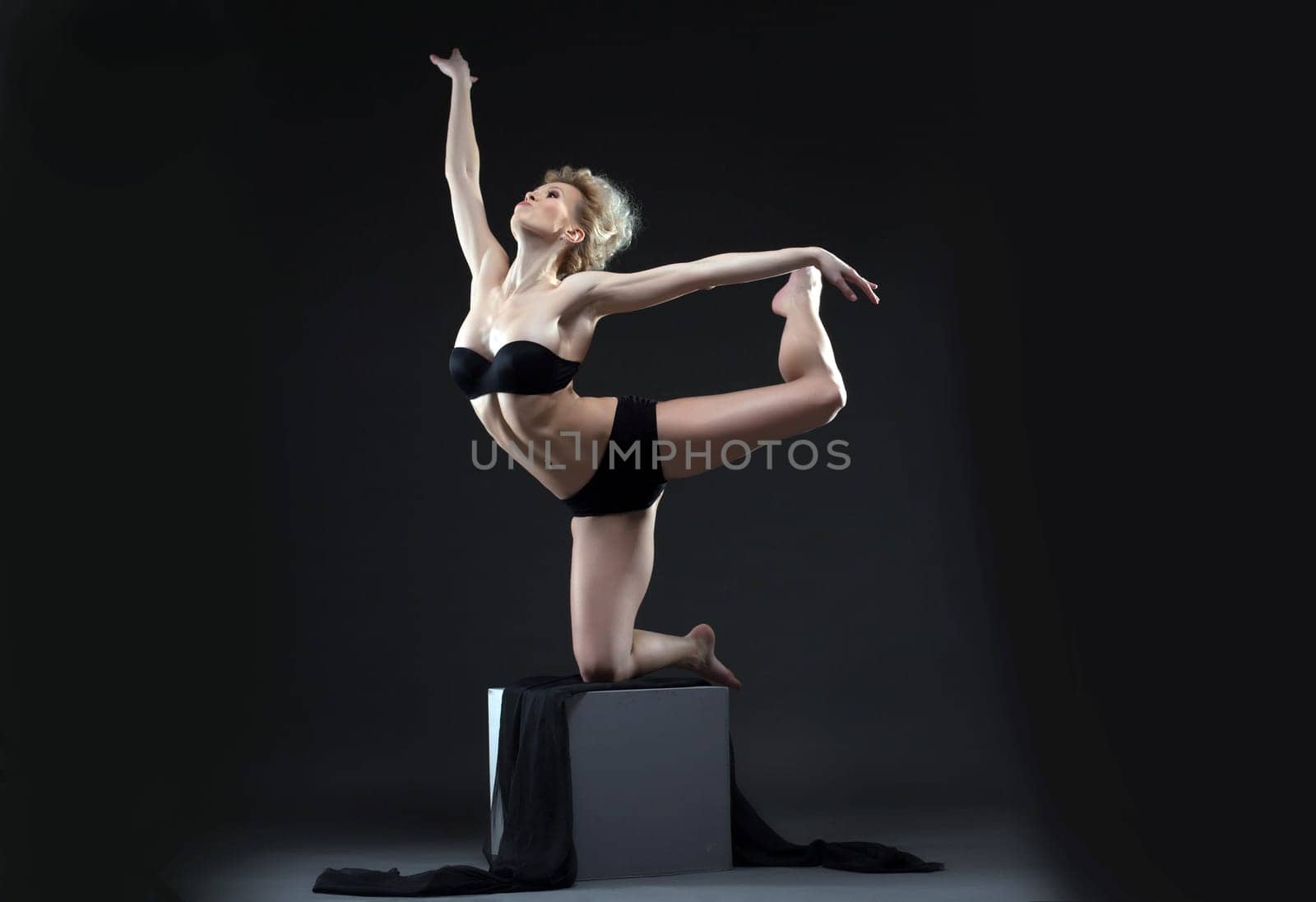 Image of seductive young dancer balancing on cube in studio